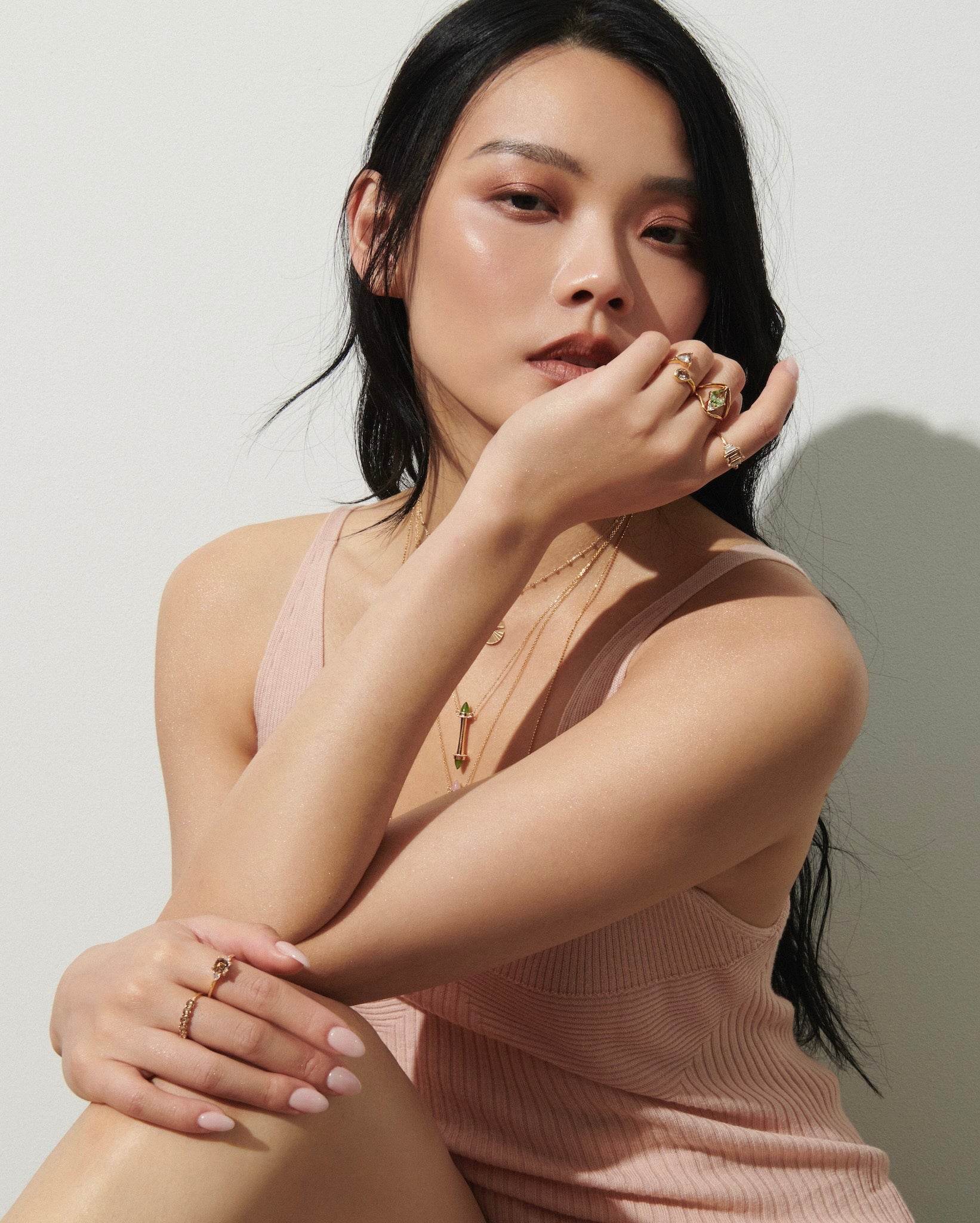 Model Sitting in Sun Against White Wall with Gold Necklaces from Vale Jewelry and One-of-a-Kind Rings Including Tourmaline Ring and 5-Stone Champagne Diamond Ring from Vale Jewelry
