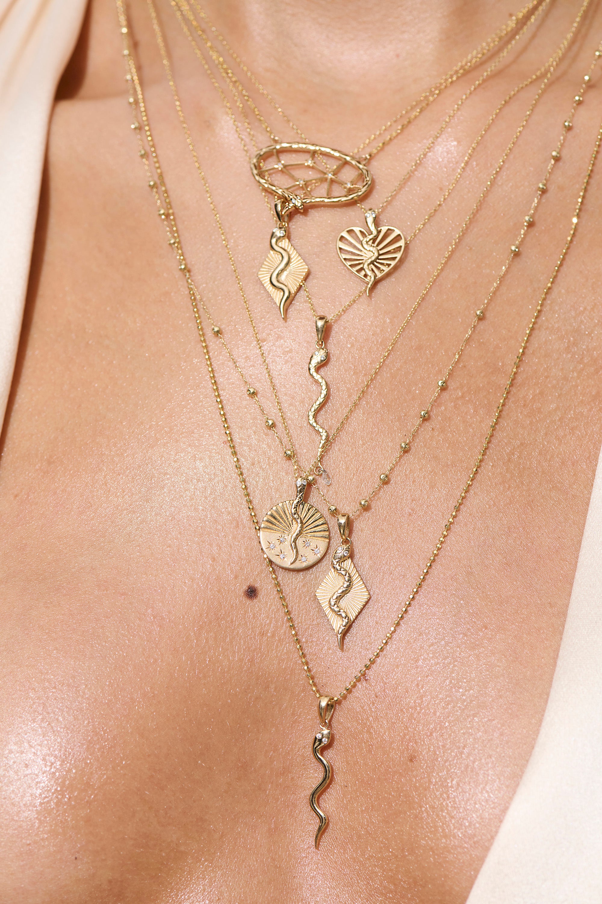 Model shot of Half Ray, Serpent, textured serpent necklace with diamond drop, textured serpent ray necklace, textured serpent half ray disc necklace, and other necklaces. Close up