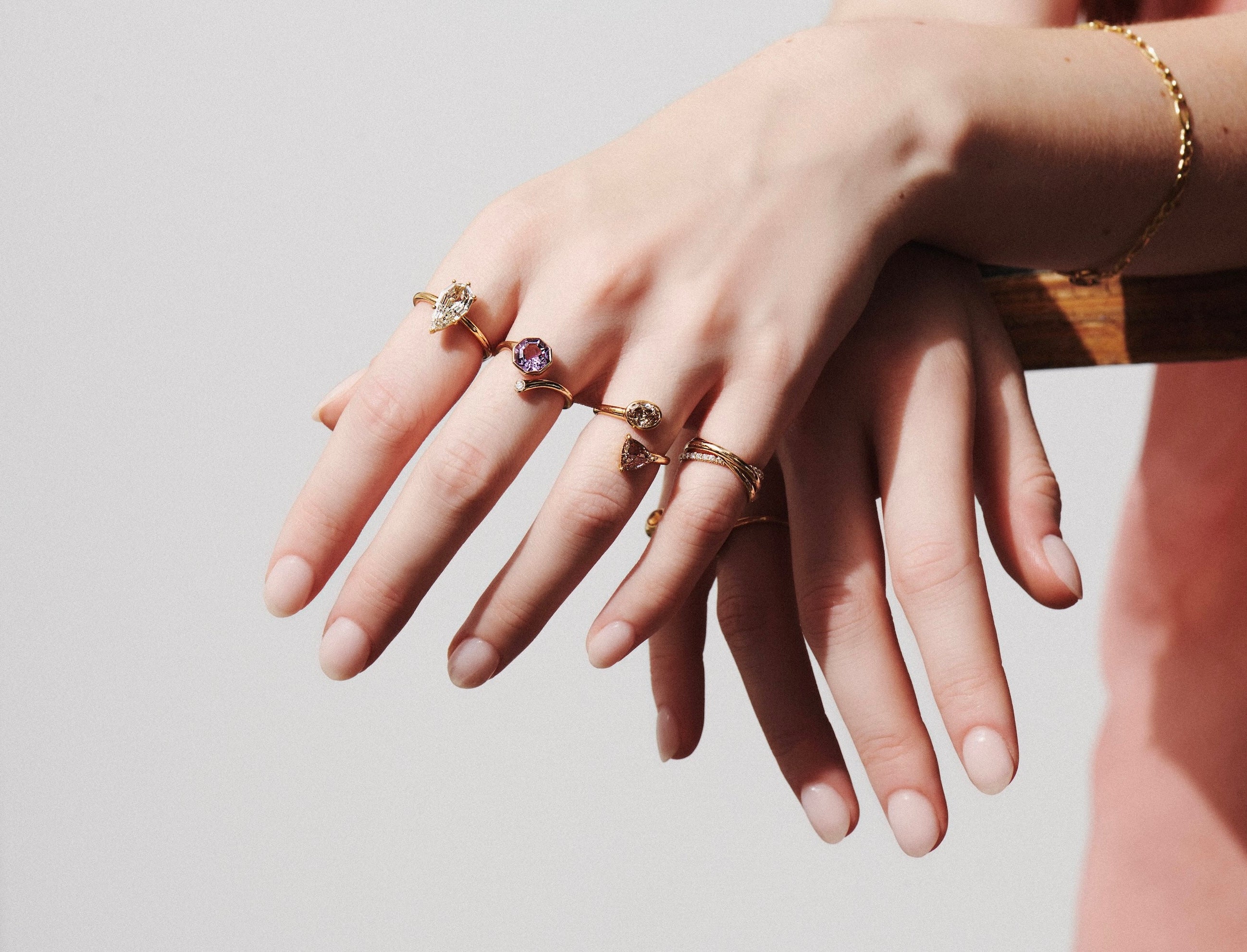 Close-up of a Model's Hand Leaning Over a Wooden Shelf Wearing Vale Jewelry One-of-a-Kind Toi et Moi Champagne Diamond Twist Ring, Amethyst Octagon & Diamond Wrap Ring, One-of-a-Kind 1.50 Carat Step Cut Pear Shape Solitaire Diamond RIng, Sintra Rolling Ring with White Diamonds