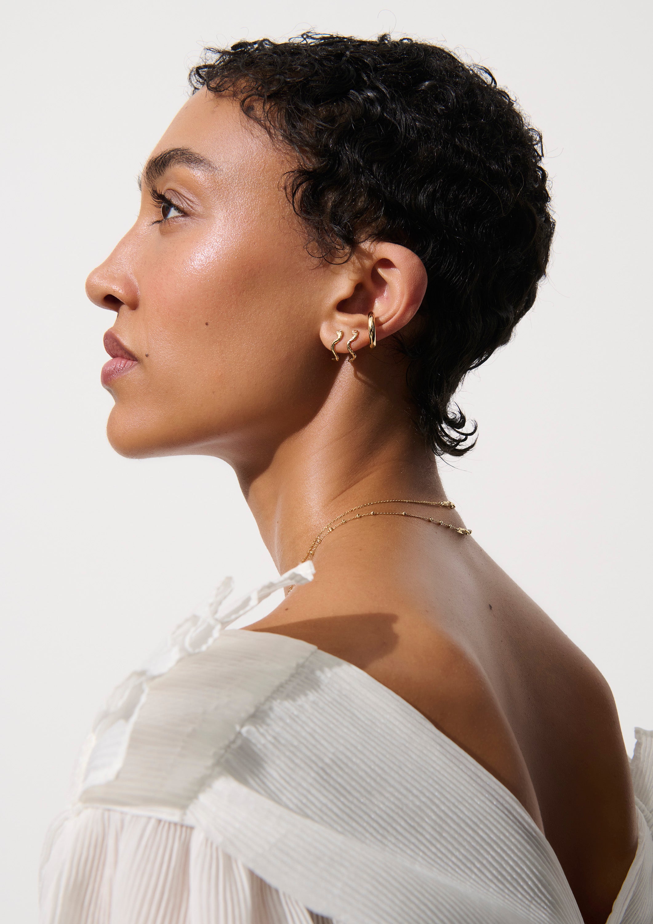 Alt="Vale Jewelry model in profile wearing serpent half hoops and other jewelry"