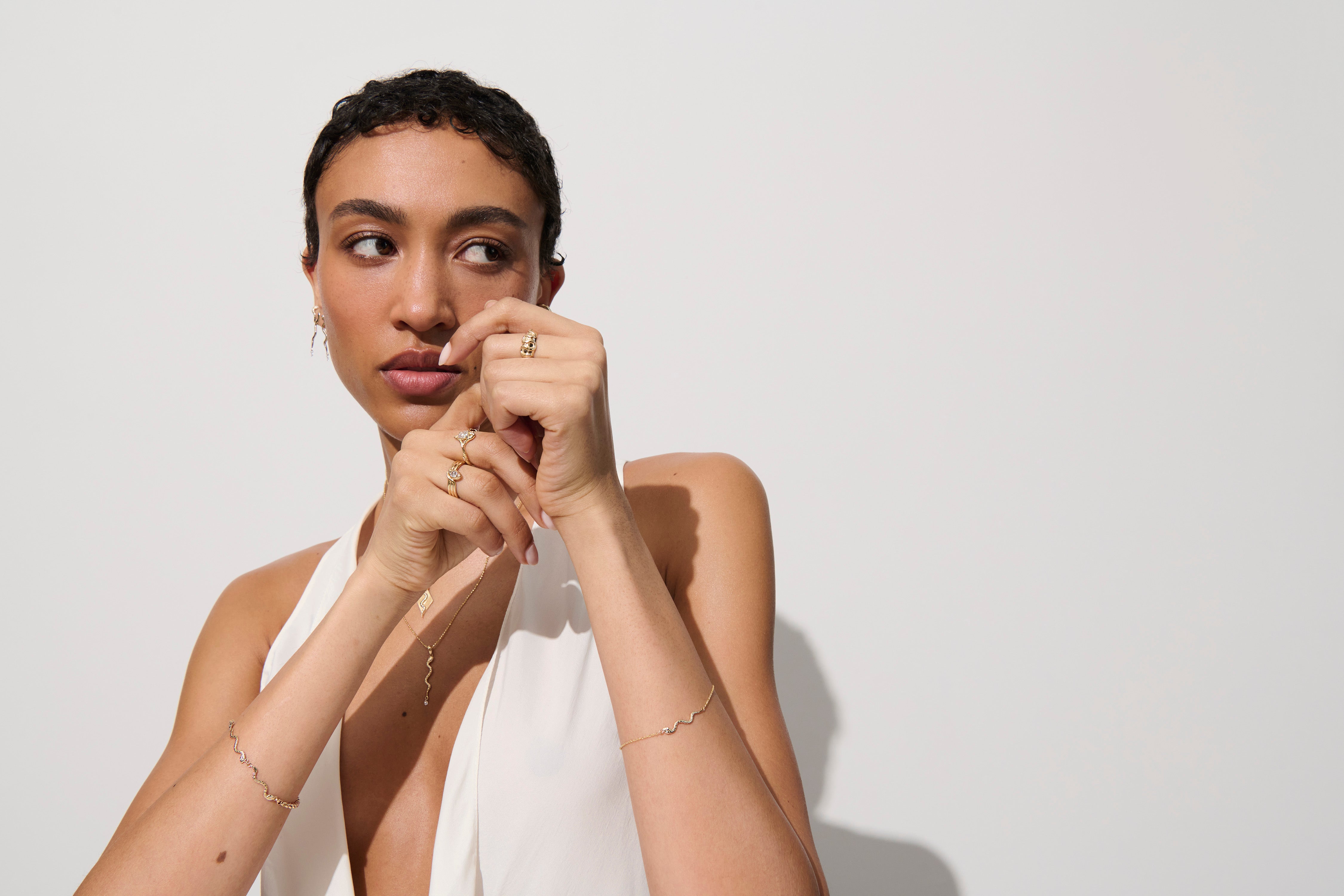 Alt="Vale Jewelry model wearing gold snake bracelet on white background, hands raised, wearing domed serpent ring"