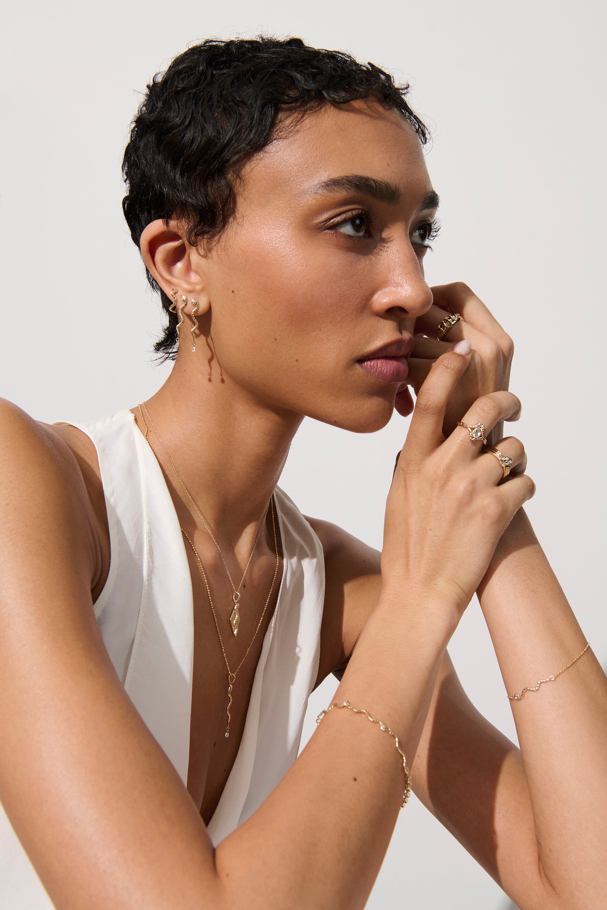 Alt="Vale Jewelry model wearing gold bracelet, textured serpent earrings with diamond drops, textured serpent with diamond drop necklace, and other jewelry"