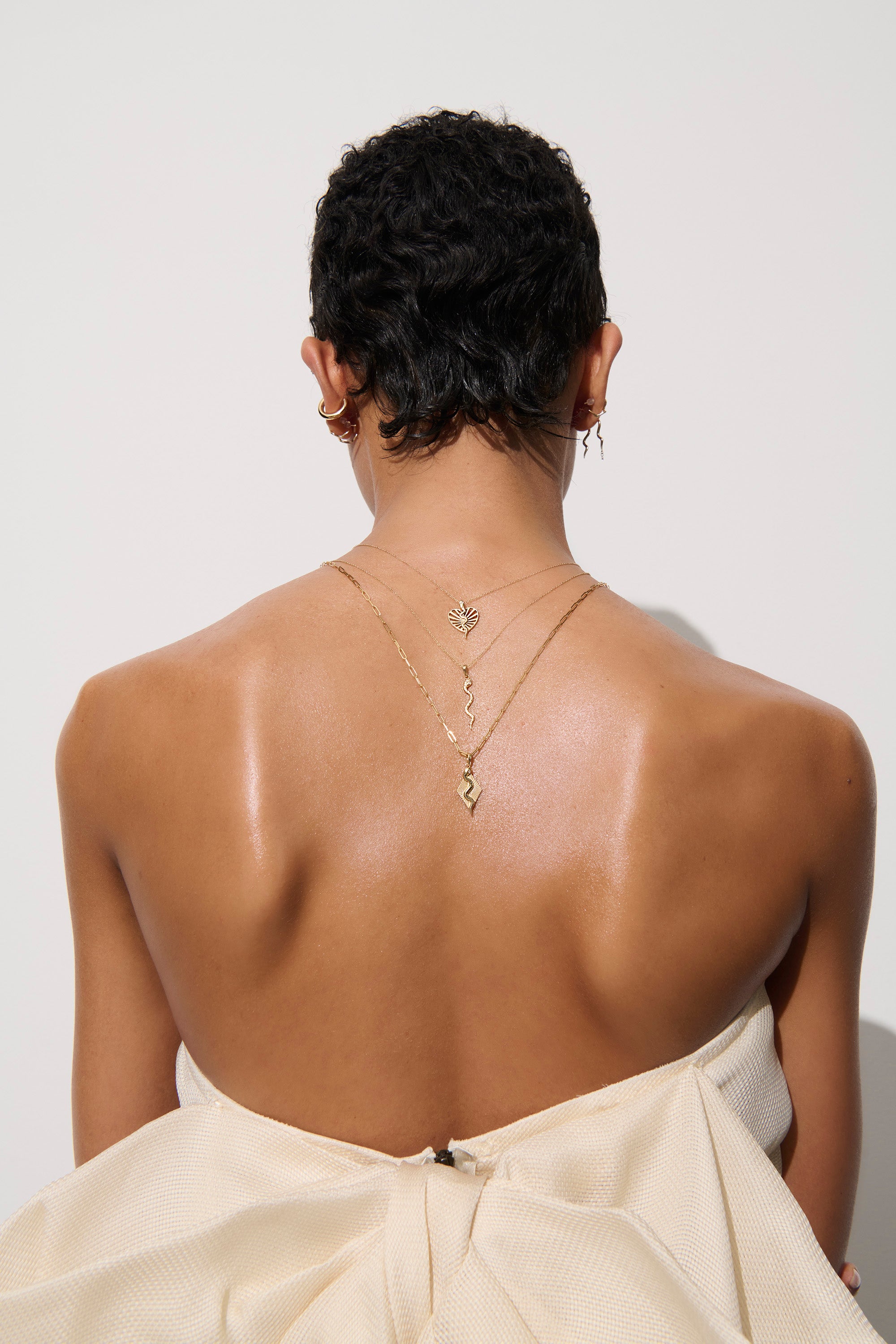 Model in white strapless dress facing away from the camera wearing textured serpent necklace
