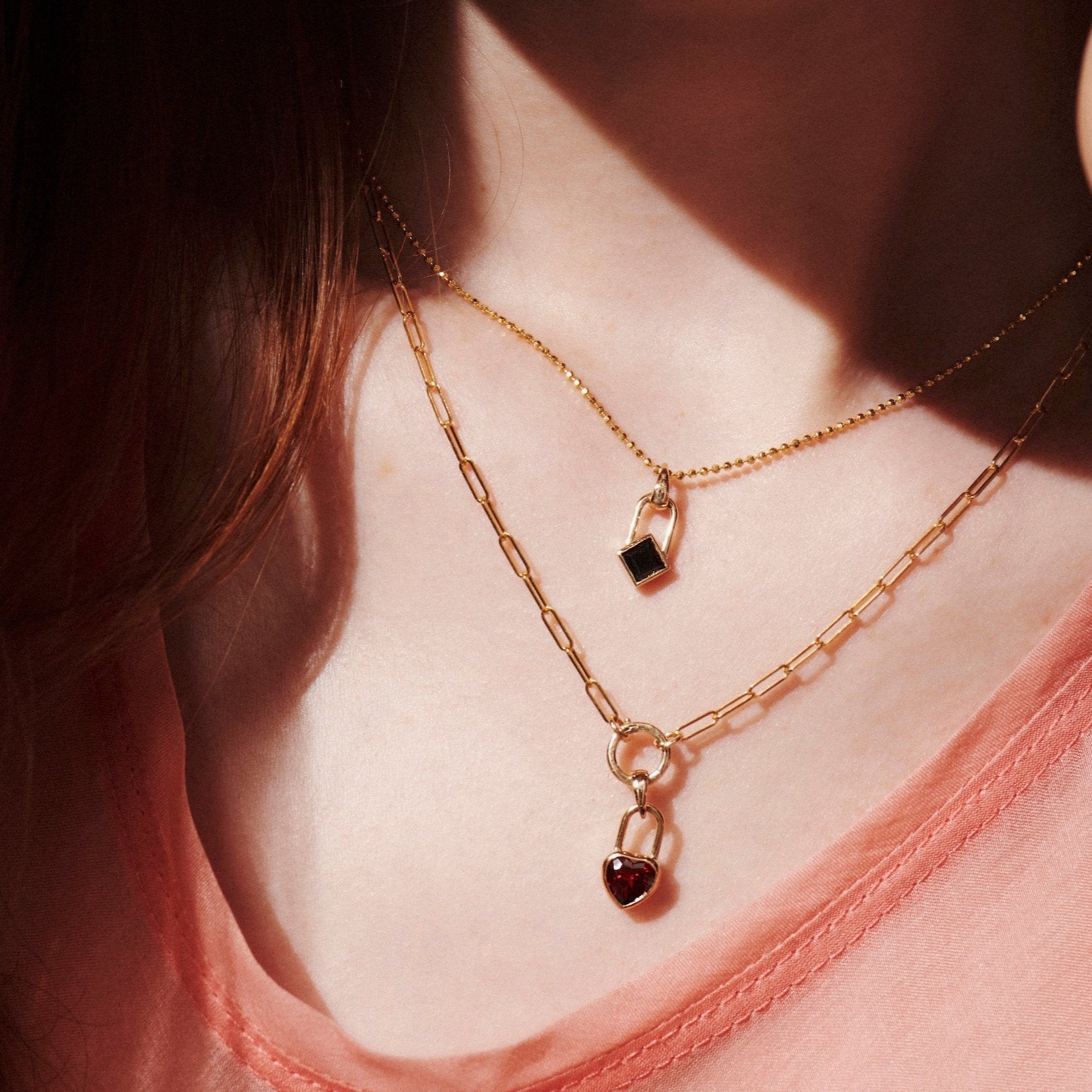 Model wearing Vale Jewelry Heart Lock Garnet Necklace in Yellow Gold and Square Lock Black Onyx Necklace