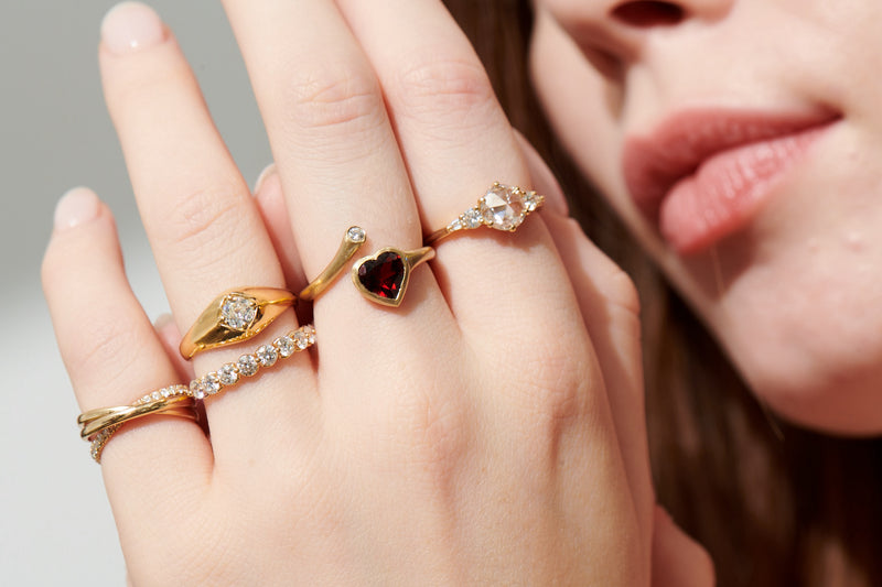 Close-up Image of Model Wearing Vale Jewelry Agata Ring, Cymbeline Ring, Garnet Heart and Diamond Twist Ring, Amour Fou Ring with Rose Cut Diamonds and Sintra Rolling Ring with White Diamonds