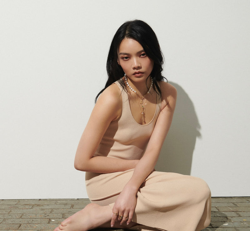 Model Sitting on Brick Floor Against White Background Wearing Amphora Scroll Necklaces with Jade and Rose Quartz from Vale Jewelry