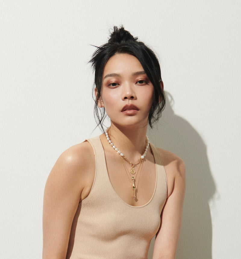 Model Sitting on Brick Floor Against White Background Wearing Amphora Scroll Necklaces with Rose Quartz and with Jade from Vale Jewelry