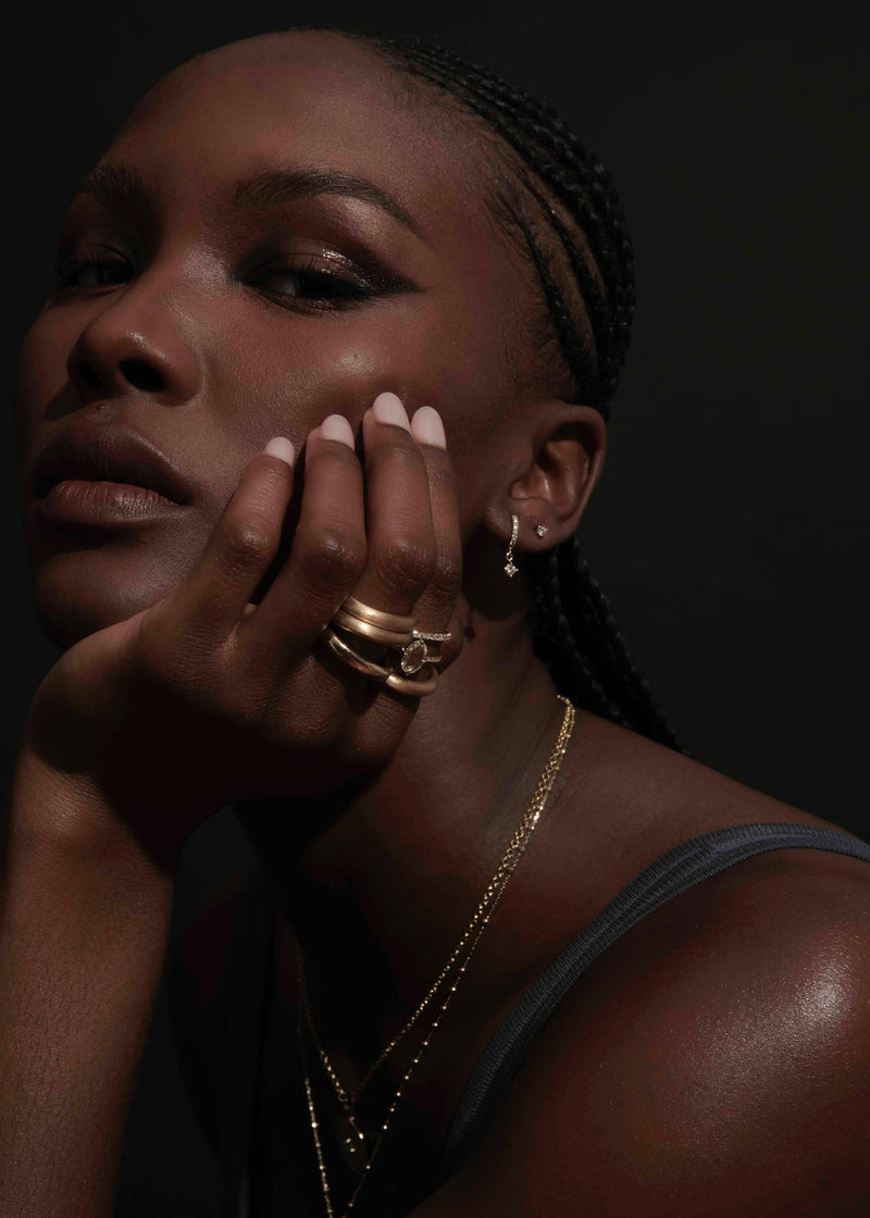 Model Wearing Pavé Huggie Hoop Earrings with Princess Cut Diamonds and Chunky Stack of Gold Barrel Rings from Vale Jewelry