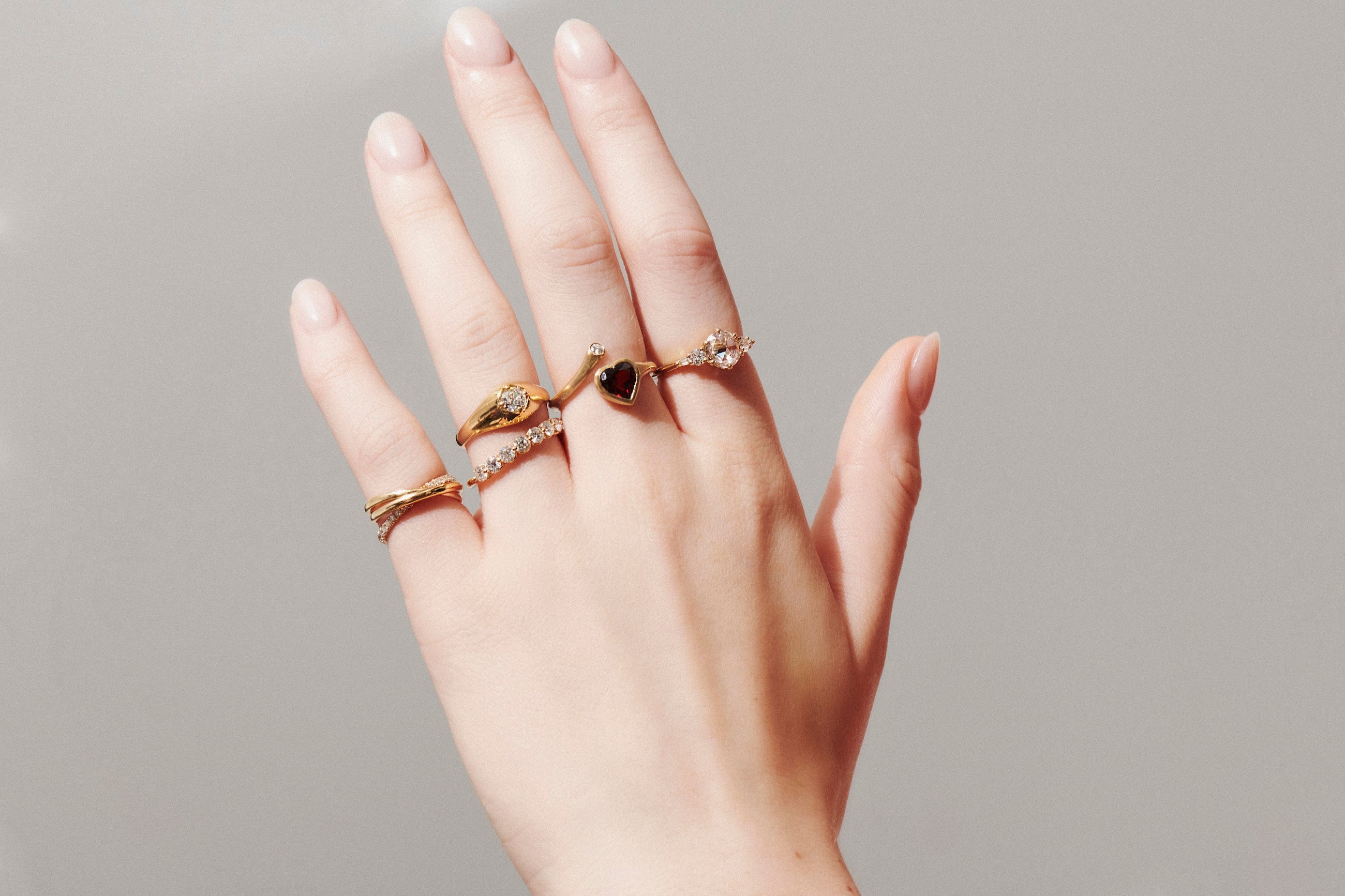Close-up Image of Model's Open Hand Wearing Vale Jewelry Agata Ring, Cymbeline Ring, Garnet Heart and Diamond Twist Ring, Amour Fou Ring with Rose Cut Diamonds and Sintra Rolling Ring with White Diamonds