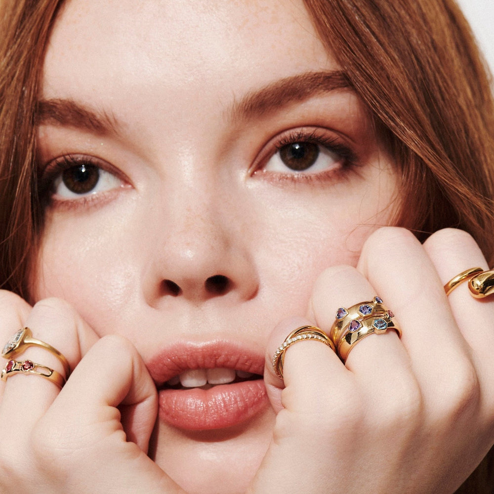 Model with Both Hands Under Chin Looking Up Wearing Vale Jewelry Rings Including Mixed Shape Blue Sapphire Dome Ring, Mixed Shape Multi-Stone Dome Ring, Twist Ring, Sintra Rolling Ring, Mixed Shape Multi-Stone Open Band Lock Ring, and One-of-a-Kind Cushion Rose Cut Bezel Set Diamond Ring