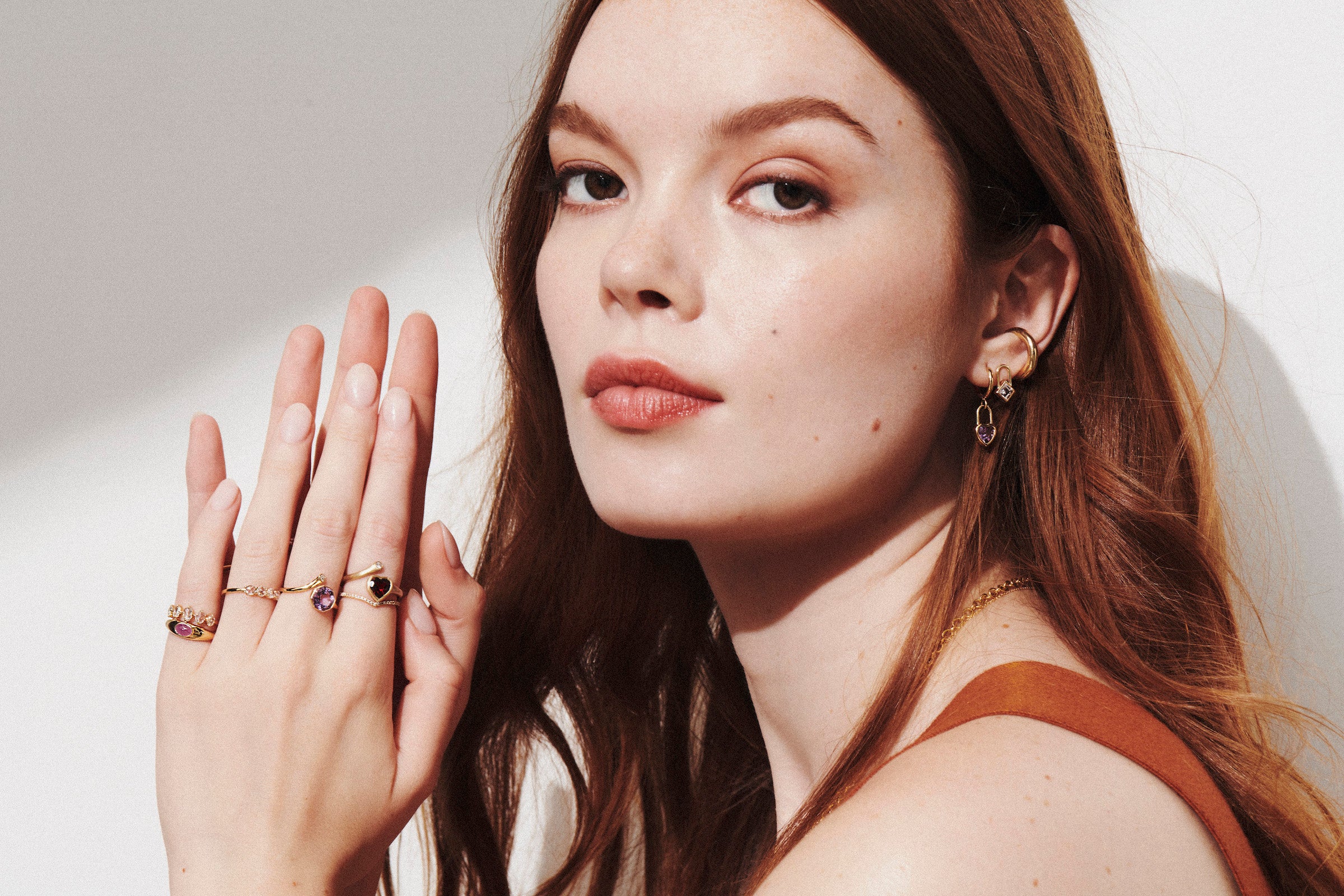 Model With Hands Up Wearing Ring Stack from Vale Jewelry Including Garnet Heart and Diamond Wrap Ring and Amethyst and Diamond Wrap Ring and Morganite Square Lock and Heart Amethyst Huggie Earrings 