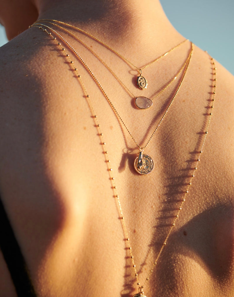 Model Wearing Layers of Gold Necklaces Including Figa Amulet Necklace, Protection Medallion Necklace, Starlight Amulet Necklace from Vale Jewelry