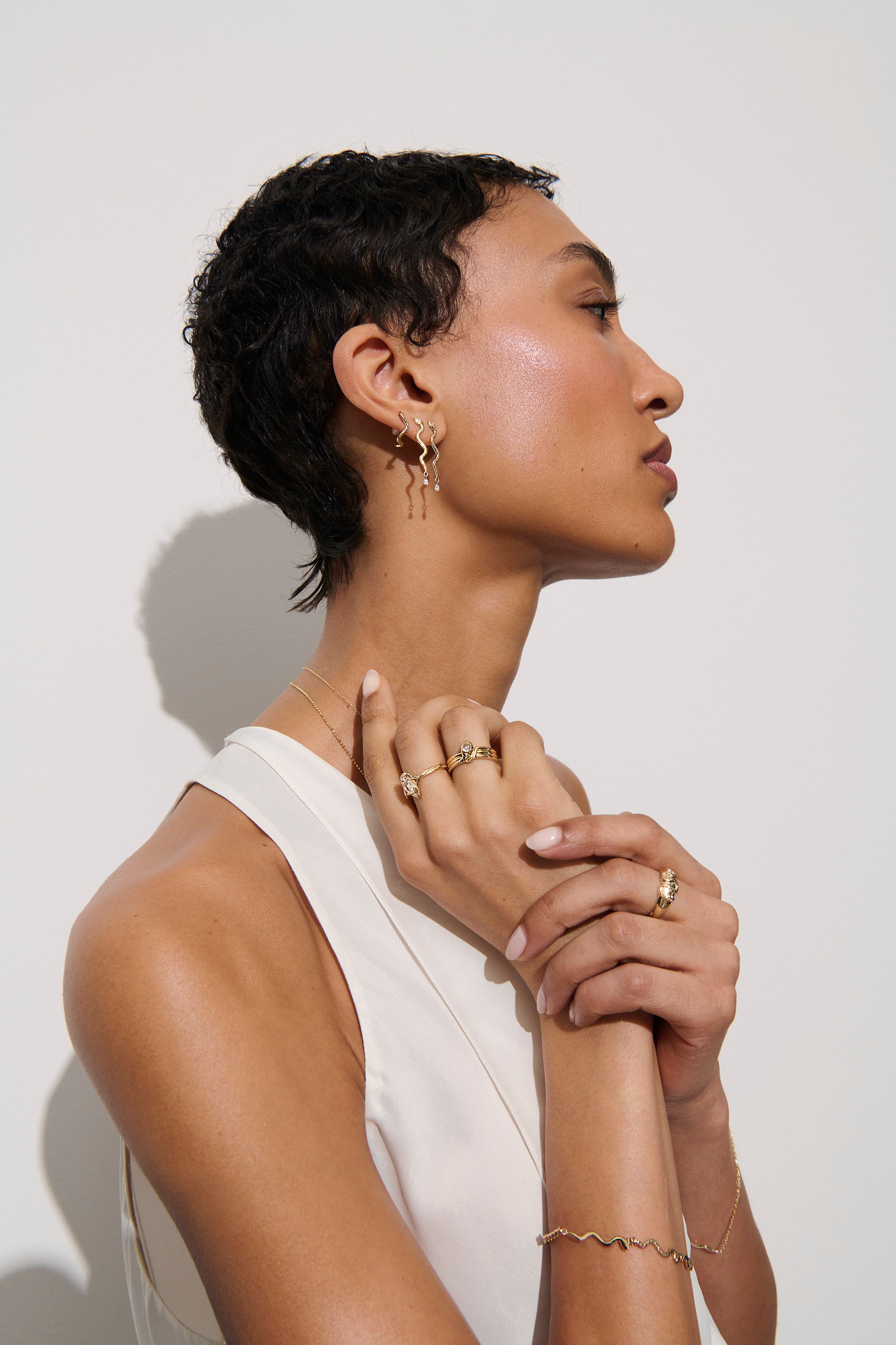Alt="Vale Jewelry model in profile wearing textured serpents bracelet, serpent earrings with diamond drops, with gold domed serpent ring"