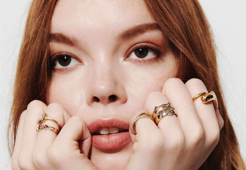 Model with Both Hands Under Chin Looking Up Wearing Vale Jewelry Rings Including Mixed Shape Blue Sapphire Dome Ring, Mixed Shape Multi-Stone Dome Ring, Twist Ring, Sintra Rolling Ring, Mixed Shape Multi-Stone Open Band Lock Ring, and One-of-a-Kind Cushion Rose Cut Bezel Set Diamond Ring