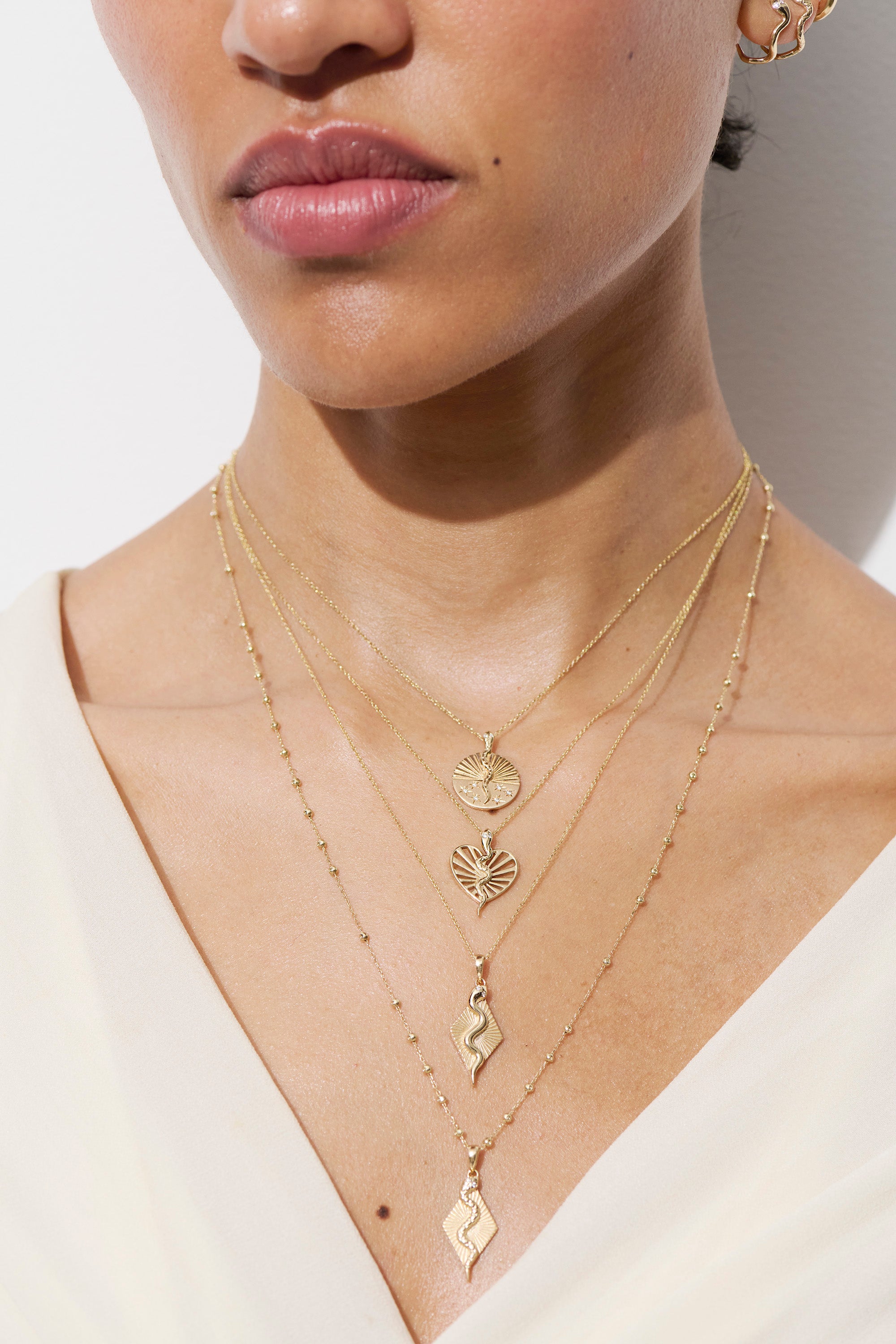 Alt="Vale Jewelry model wearing serpent ray necklace, textured serpent ray necklace and other necklaces close up with a white shirt on"