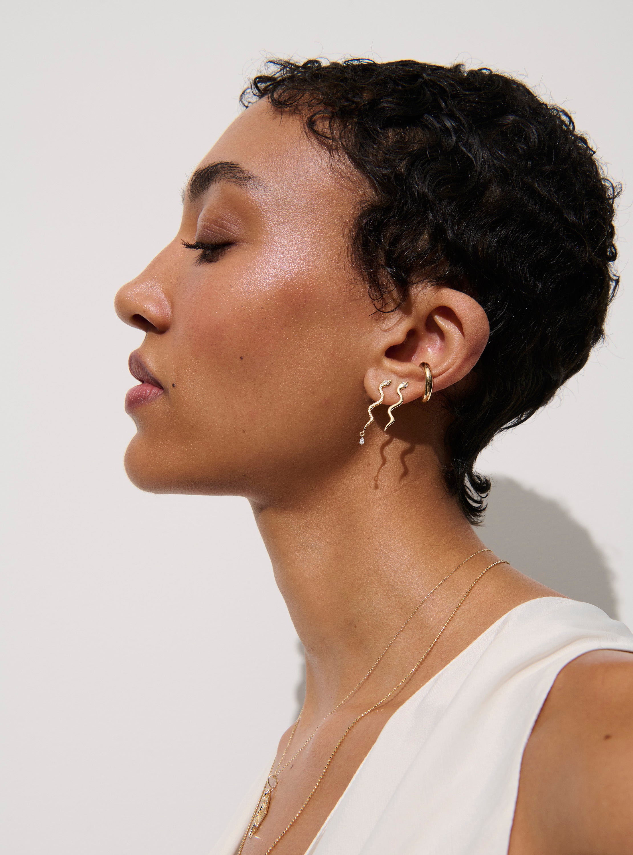 Alt="Vale Jewelry woman wearing gold textured serpent earrings with diamond drops, serpent earrings and a necklace"