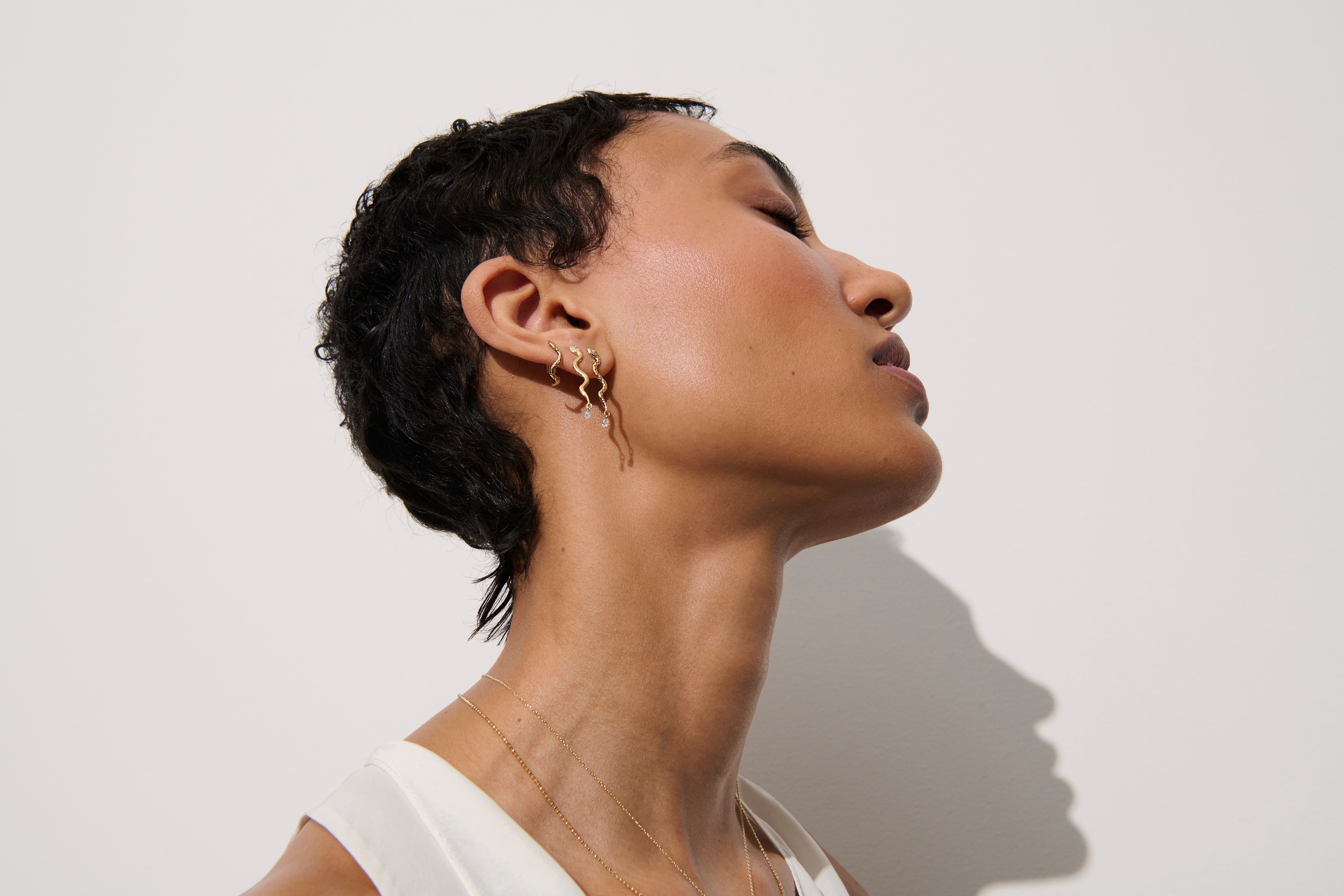 Alt="Vale Jewelry textured serpent half hoops earrings on model next serpent earrings with diamond drop next to other earrings"